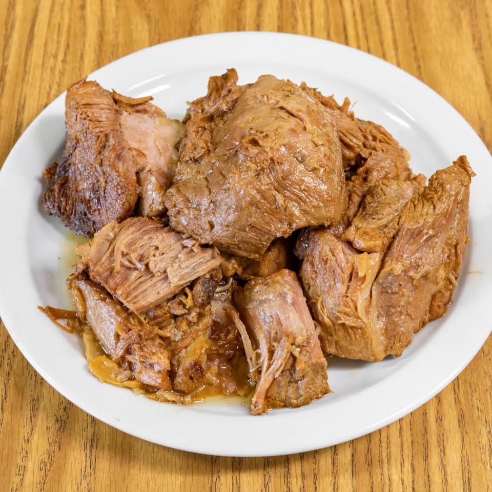 A white plate filled with generous portions of tender, juicy, slow-cooked carnitas on a wooden table.