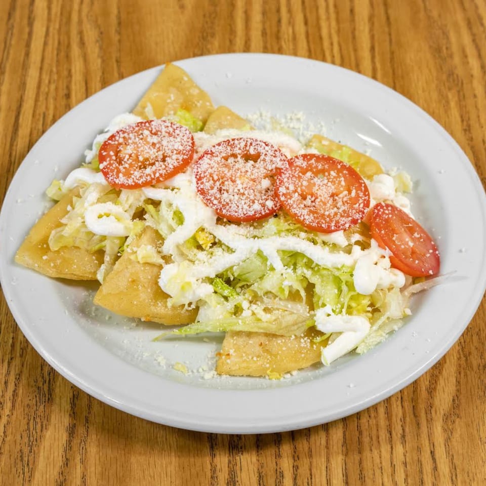 Golden fried tortillas topped with shredded lettuce, sliced tomatoes, sour cream, and crumbled cheese.