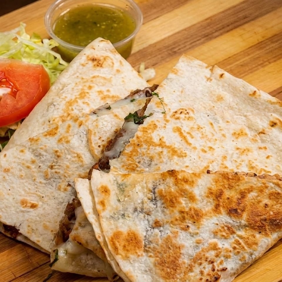 Three quesadilla slices with melted cheese and meat, served with lettuce, tomato, and green salsa.